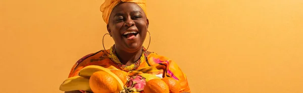 Sorrindo mulher afro-americana de meia idade com frutas exóticas em laranja, bandeira — Fotografia de Stock