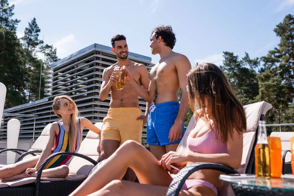 Multiehtnic friends in swimming trunks toasting with beer outdoors — Stock Photo