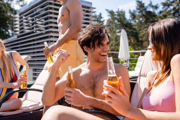 Hombre con cerveza mostrando sí gesto cerca amigo en traje de baño al aire libre - foto de stock