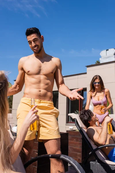 Muslim man in swimwear talking to friend with beer on blurred foreground outdoors — Stock Photo