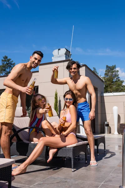 Multiethnic friends holding beer on deck chairs outdoors — Stock Photo