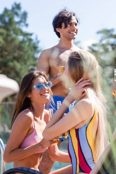 Mulheres sorridentes em maiôs segurando cerveja perto de amigo ao ar livre — Fotografia de Stock