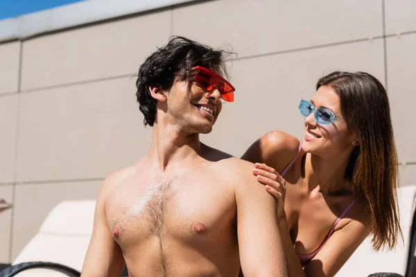 Sorrindo mulher olhando para amigo sem camisa em óculos de sol ao ar livre — Fotografia de Stock