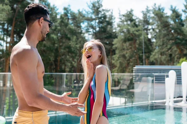 Excited woman in swimsuit standing near muslim friend and swimming pool — Stock Photo