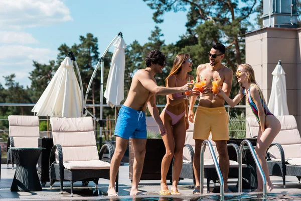 Multiethnische Menschen in Badebekleidung prosten sich in der Nähe des Schwimmbades mit Cocktails zu — Stockfoto