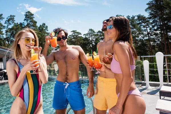 Positive interracial friends drinking cocktails near swimming pool — Stock Photo