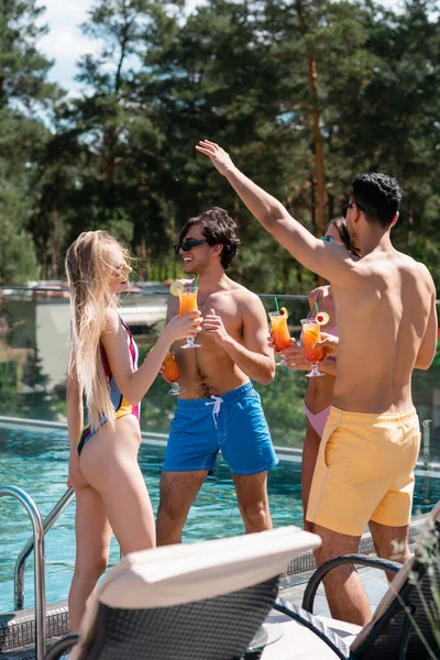 Multiethnic people in swimwear holding cocktails near swimming pool during vacation — Stock Photo