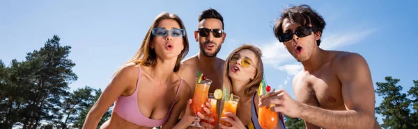 Low angle view of excited interracial people in swimwear holding cocktails during weekend, banner — Stock Photo