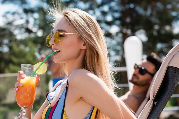 Жінка в сонцезахисних окулярах і купальнику п'є коктейль на відкритому повітрі — стокове фото