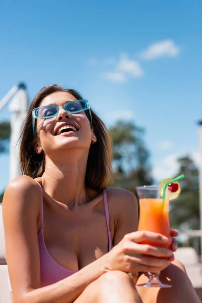 Cheerful woman in swimsuit holding blurred cocktail outdoors — Stock Photo