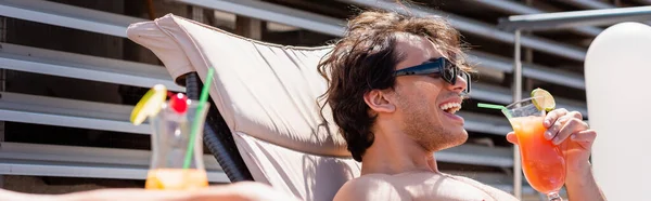 Homme positif dans des lunettes de soleil tenant cocktail avec paille à boire sur chaise longue, bannière — Photo de stock