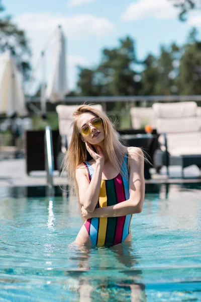 Hübsche Frau im gestreiften Badeanzug steht im Pool im Freien — Stockfoto
