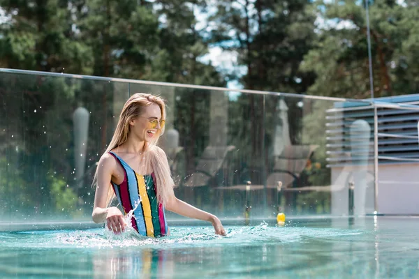 Молода жінка посміхається, розбризкуючи воду в басейні — стокове фото