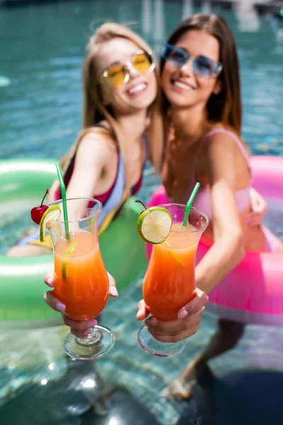 Selective focus of cocktails glasses in hands of pretty women in swimming pool — Stock Photo