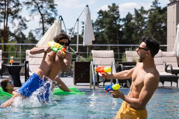 Aufgeregter arabischer Mann spielt Wasserschlacht mit Freunden im Pool — Stockfoto