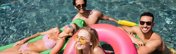 Fröhliche interrassische Freunde lachen, während sie sich im Schwimmbad ausruhen, Banner — Stockfoto