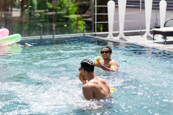 Uomo sorridente in occhiali da sole trascorrere del tempo con l'amico arabo in piscina — Foto stock