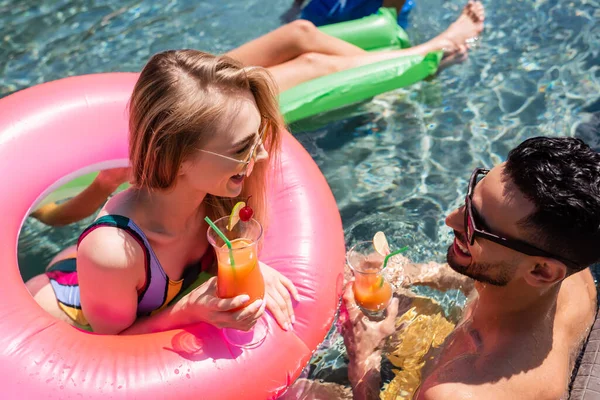 Mulher feliz conversando com o homem árabe enquanto relaxa com coquetéis na piscina — Fotografia de Stock