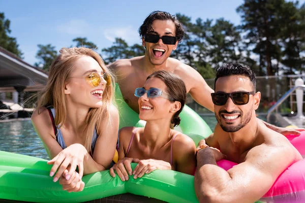 Amigos multiétnicos alegres que se divertem no colchão inflável na piscina — Fotografia de Stock