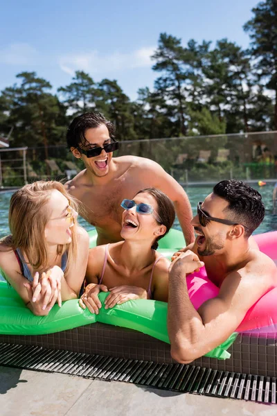 Amigos multiétnicos alegres que ríen en colchón inflable en piscina — Stock Photo