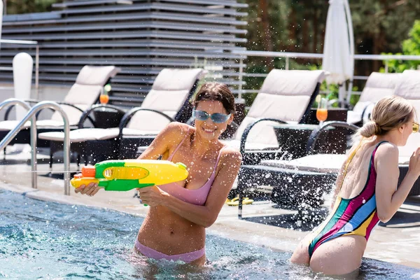 Femme gaie jouant avec pistolet à eau proche ami dans la piscine — Photo de stock