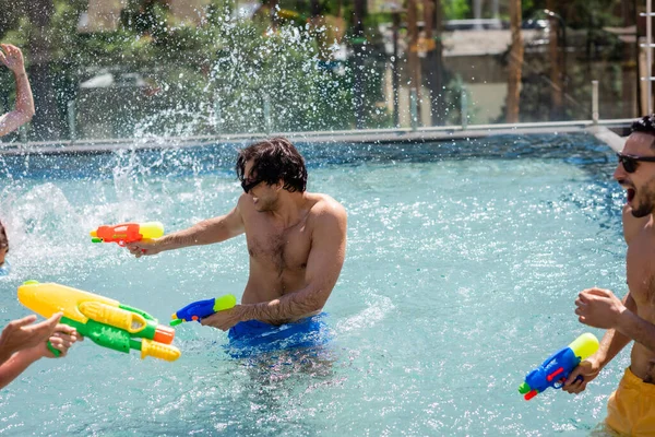 Excited multiethnic friends fighting on water guns in swimming pool — Stock Photo