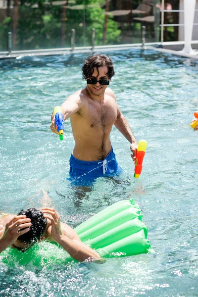 Joven disfrutando de batalla con pistola de agua árabe amigo en la piscina - foto de stock