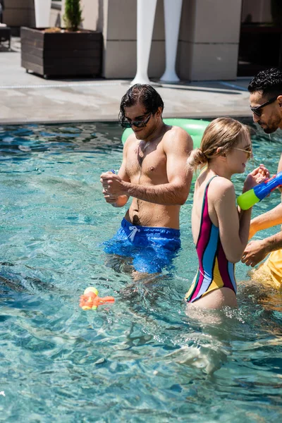 Багатонаціональні чоловіки з молодою жінкою грають з водяними гарматами в басейні — стокове фото