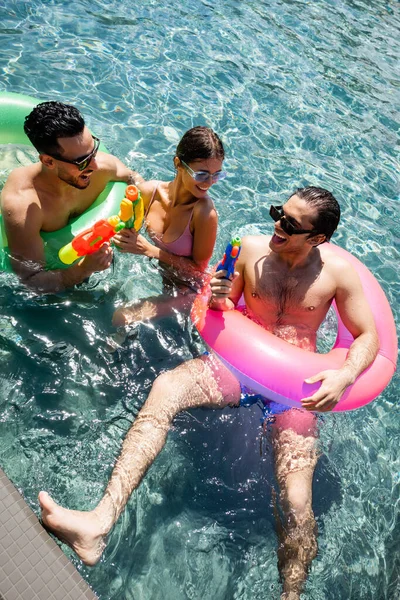 Веселі багатокультурні друзі відпочивають у басейні з водяними гарматами та пливуть кільцями — стокове фото