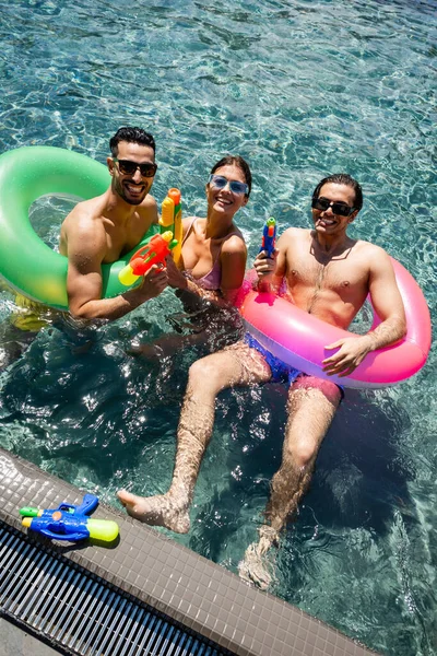 Hochwinkelaufnahme von glücklichen interrassischen Freunden mit Schwimmringen und Wasserpistolen im Pool — Stockfoto