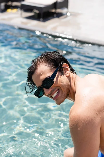 Jovem sem camisa homem em óculos de sol sorrindo perto da piscina — Fotografia de Stock