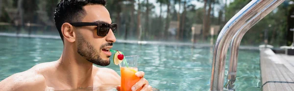 Молодой мусульманин в солнцезащитных очках пьет коктейль в бассейне, баннер — стоковое фото