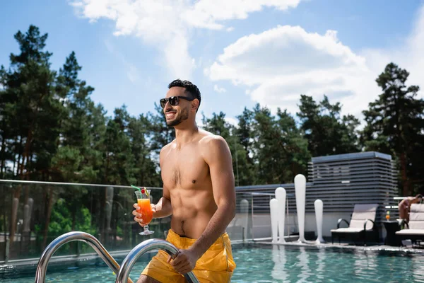 Hombre musulmán feliz celebración de cóctel mientras está de pie en la escalera de la piscina - foto de stock