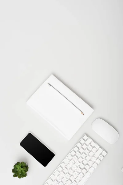 Vue du haut du smartphone avec écran blanc près de la petite usine, clavier et ordinateur portable avec crayon isolé sur blanc — Photo de stock