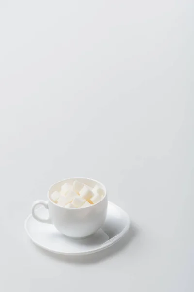 Sugar cubes in cup with saucer on white — Stock Photo