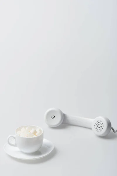 Zuckerwürfel in Tasse mit Untertasse in der Nähe von Retro-Telefon auf weiß — Stockfoto