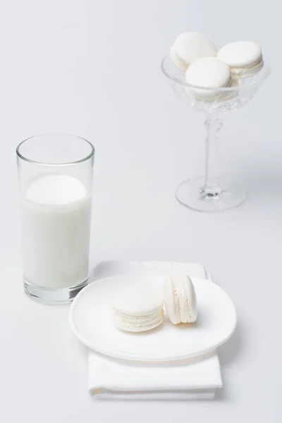 Leckere Macarons auf Teller in der Nähe von Glas Milch auf weiß — Stockfoto