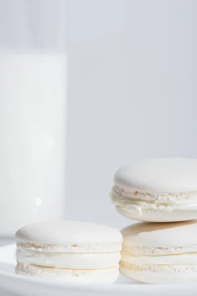 Close up view of tasty macarons near blurred glass of milk isolated on white — Stock Photo