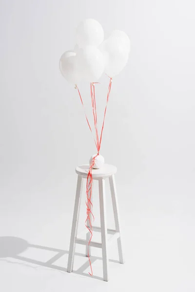 Lightweight balloons above stool with ball of thread on white — Stock Photo