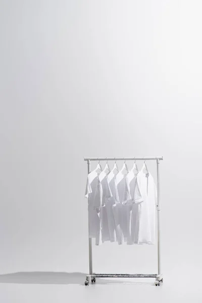 Collection of stylish t-shirts hanging on clothes rack isolated on grey — Stock Photo