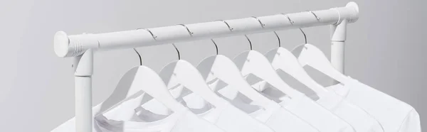 Coleção de camisetas brancas penduradas no rack de roupas isolado em cinza, banner — Fotografia de Stock