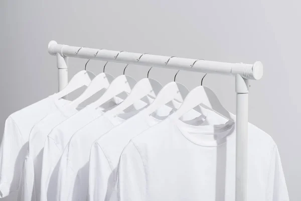 Collection of trendy white t-shirts hanging on clothes rack isolated on grey — Stock Photo