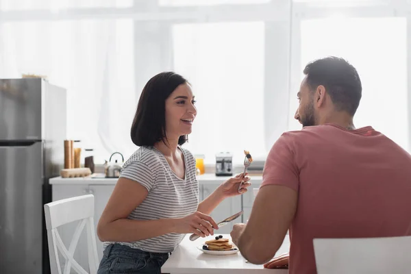 Sorrindo jovem casal comendo panquecas juntos na cozinha — Fotografia de Stock