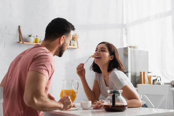 Positivo jovem mulher comer panquecas perto namorado na cozinha — Fotografia de Stock