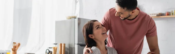 Smiling young man hugging girlfriend in kitchen, banner — Stock Photo