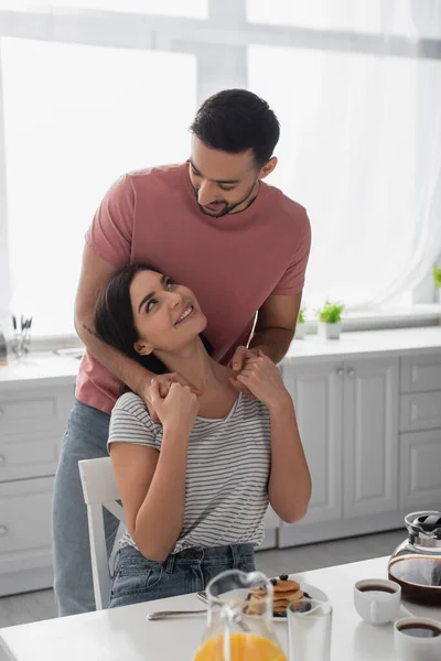 Sourire jeune couple étreignant près de la table avec petit déjeuner, café et jus d'orange dans la cuisine — Photo de stock