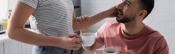 Vista recortada de la mujer joven tocando novio y sosteniendo taza con café, pancarta - foto de stock