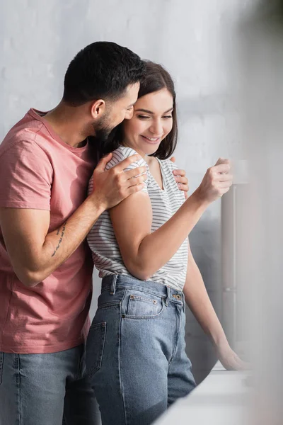 Junges verliebtes Paar umarmt sich mit Kaffeetasse in moderner Küche — Stockfoto