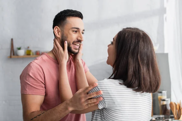 Sorridente giovane coppia che si abbraccia e si tocca con le mani in cucina moderna — Foto stock