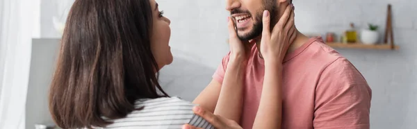 Sourire jeune femme toucher le visage du petit ami avec les mains dans la cuisine moderne, bannière — Photo de stock
